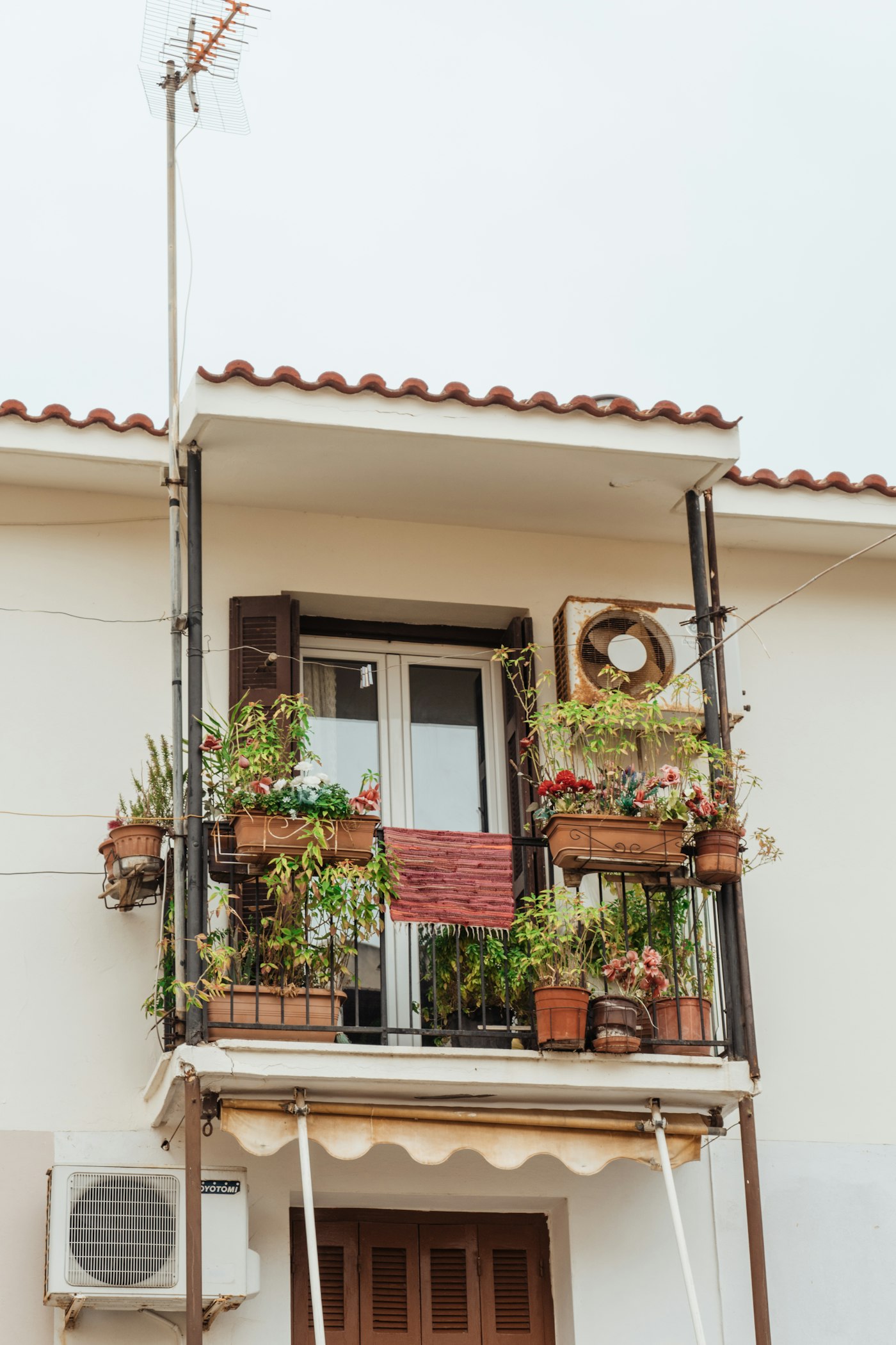 A small apartment balcony packed with potted plants against a wall-mounted air conditioning unit